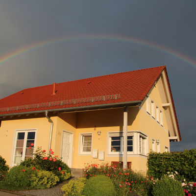 Großes hellgelbes Haus über das sich gerade ein Regenbogen spannt.