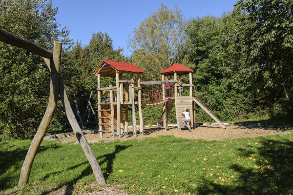 Ein Spielplatz mit einem Klettergerüst und Schaukel aus Holz.