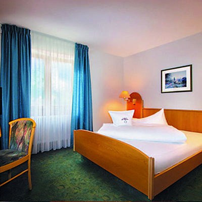 Hotelzimmer mit Doppelbett, Schreibtisch und großem Fenster mit blauen Vorhängen.