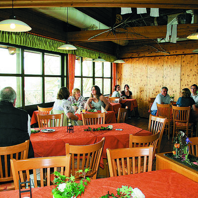 An mit rotem Tischtuch gedeckten Tischen sitzen Gäste auf Holzstühlen.