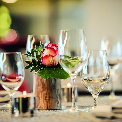 Tisch mit Wein- und Wwassergläser sowie Rosengesteck in der Mitte.
