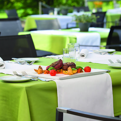 Gedeckte Tische im Außenbereich, mit grüner Tischdecke und appetitlich angerichtetem Steakgericht.