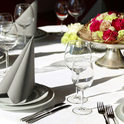 Elegnat gedeckter Tisch mit grauer Serviette, Wein- und Wassergläser sowie Blumenschmuck in der Mitte.