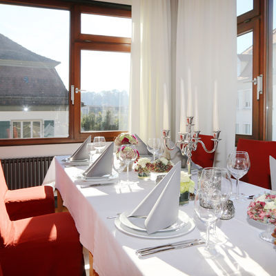 Elegant gedeckter Tisch, mit gefalteter Stoffserviette und Kerzenleuchter auf dem Tisch. Um die Tafel stehen rote Stühle.