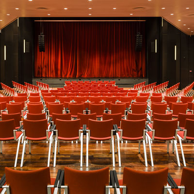 Bestuhlung der Stadthalle, Perspektive frontal auf die Bühne mit rotem Vorhang.