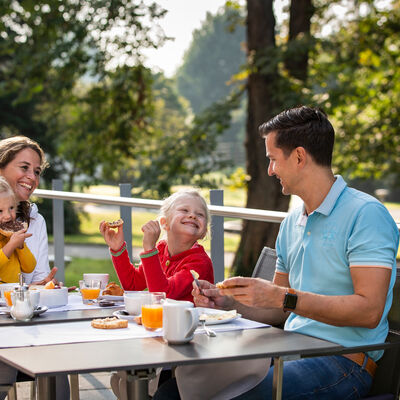 Parkrestaurant im Parkhotel Jordanbad. Eine Frau, ein Mann und zwei Kinder frühstücken im Freien.