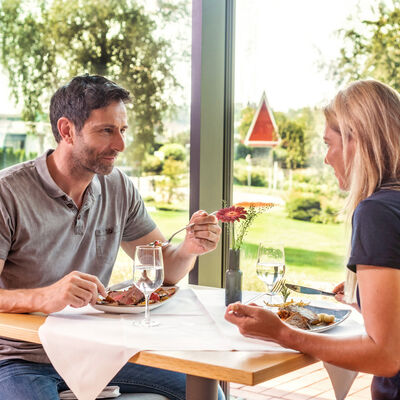 Thermenhotel Bad Buchau Hotelrestaurant. Eine Frau und ein Mann essen am Esstisch einen Hauptgericht